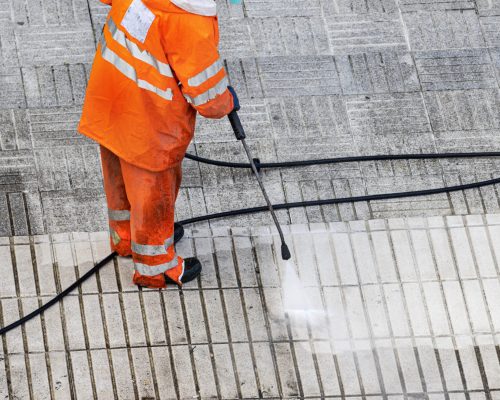 Worker cleaning a street sidewalk with pressurized water. Copy space